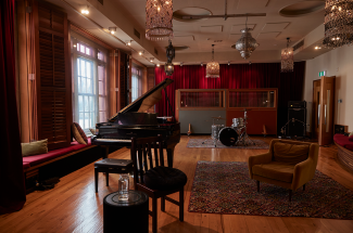 A grand piano in the middle of Roundhead Studios with a drum set in the background
